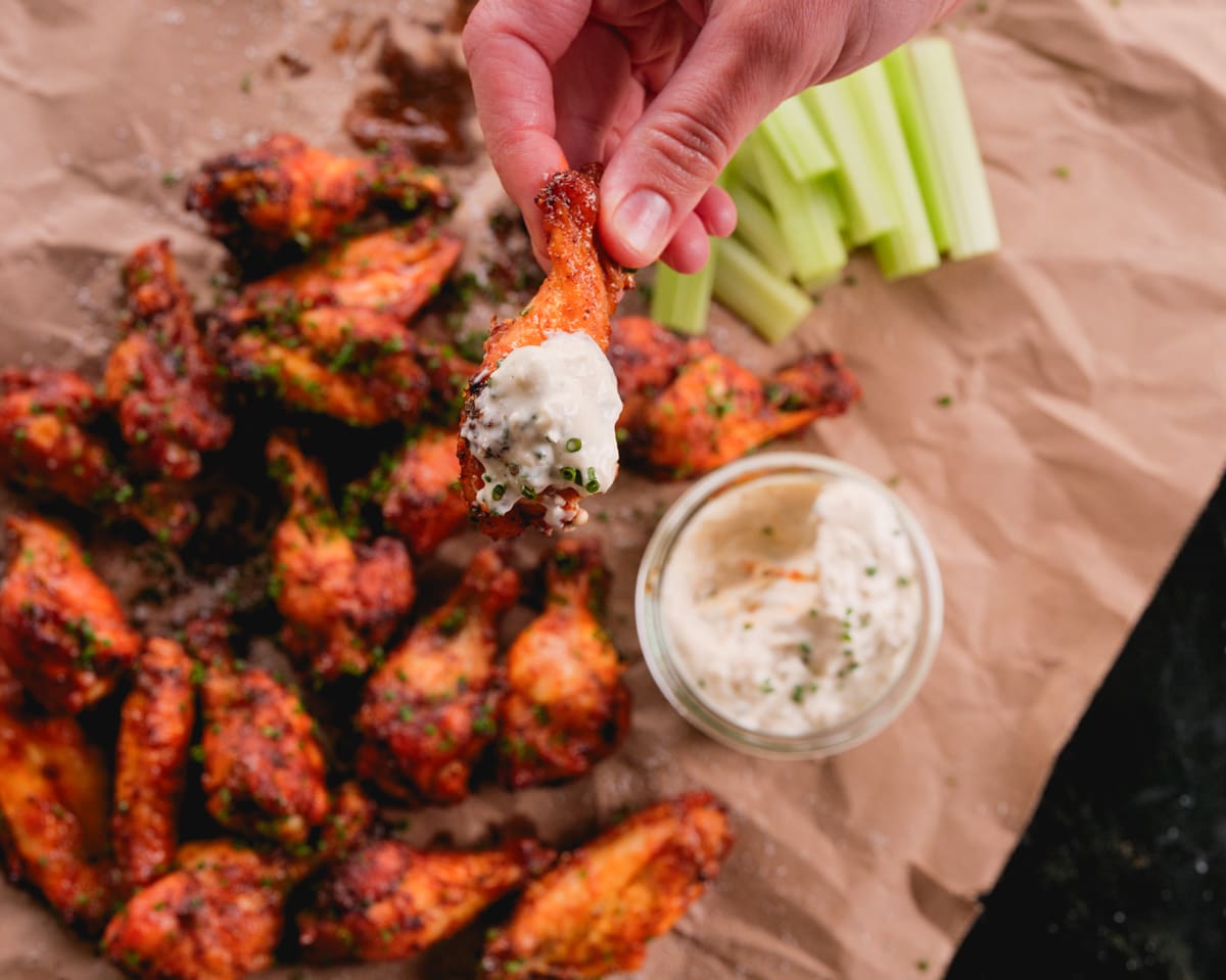 a pile of hot buffalo chicken wings with a jar of creamy blue cheese dressing.